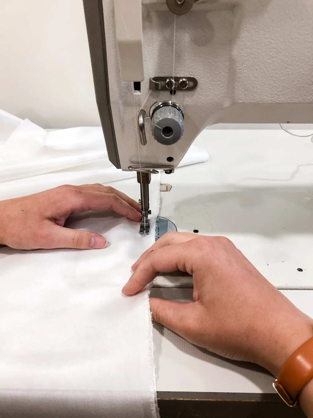 Mains de Lucie Charoy guidant un tissu blanc sous le pied d'une machine à coudre, dans l'atelier Lolette