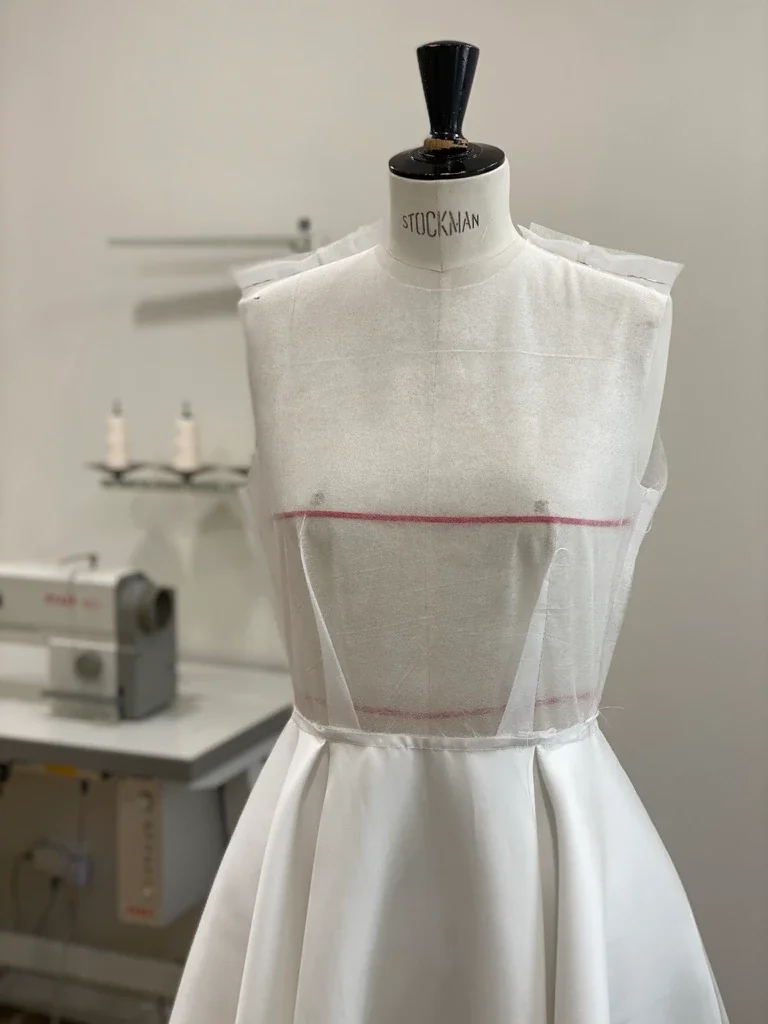 Toile d'essai d'une robe de mariée sur un mannequin de couture dans l'atelier Lolette à Gap, machine à coudre au fond