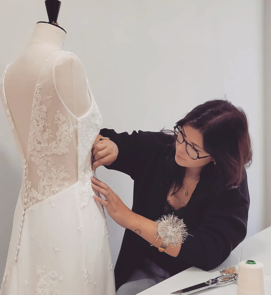 Lucie Charoy ajuste le dos en dentelle d'une robe de mariée sur un mannequin