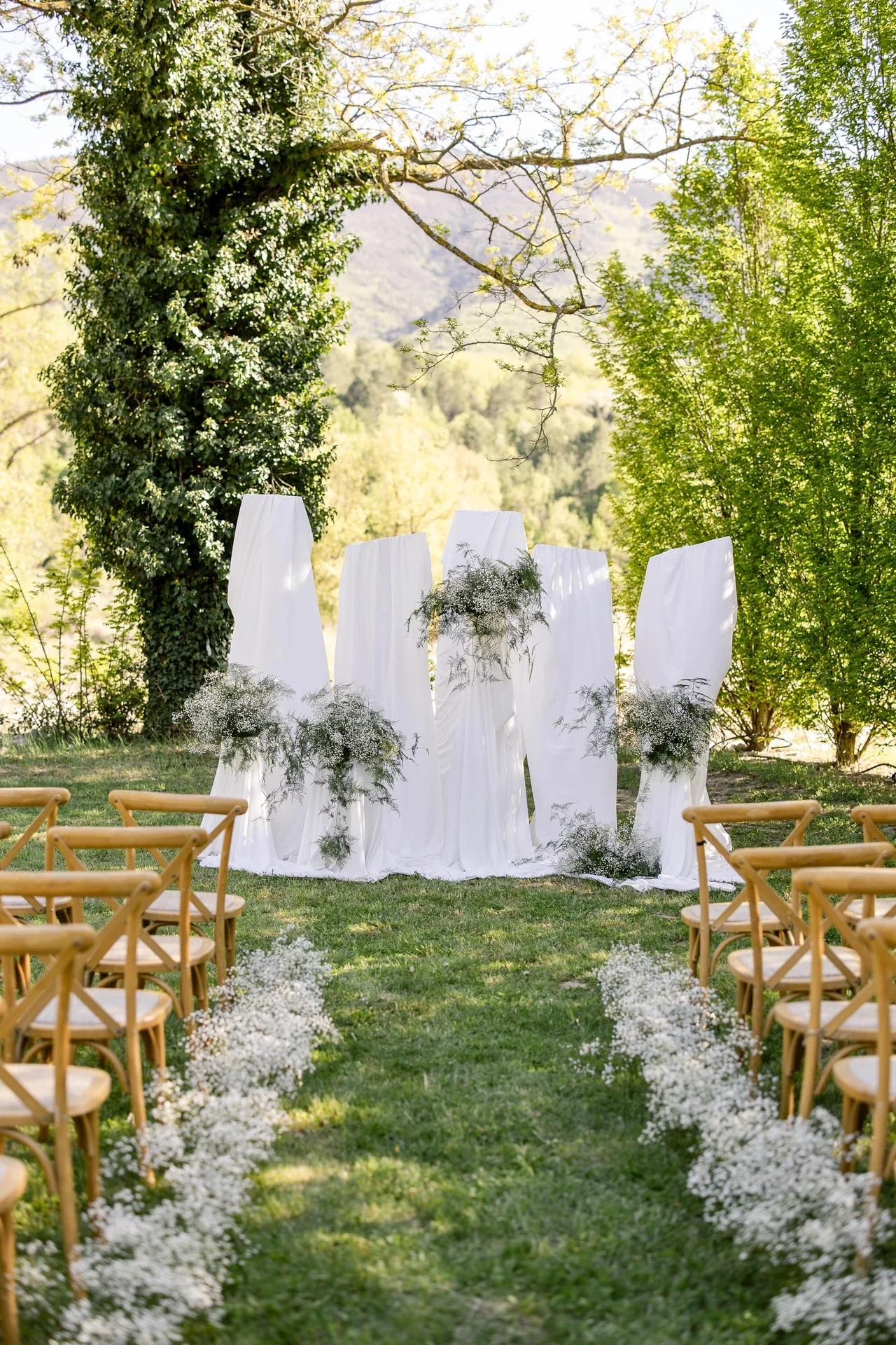 Cérémonie laïque en plein air, arche drapée de blanc et chaises en bois