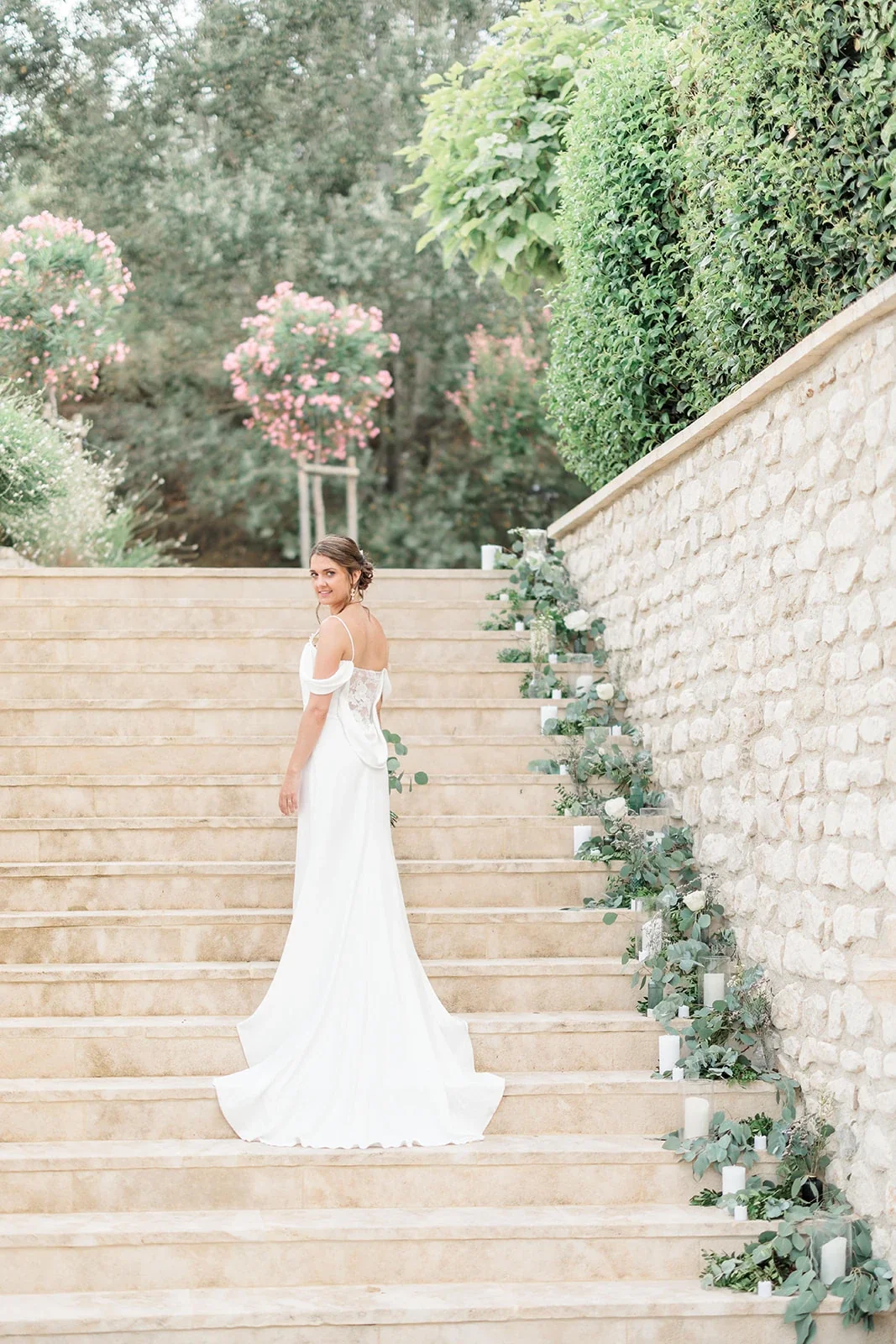 Mariée en robe à traîne posant dans un escalier de pierre fleuri