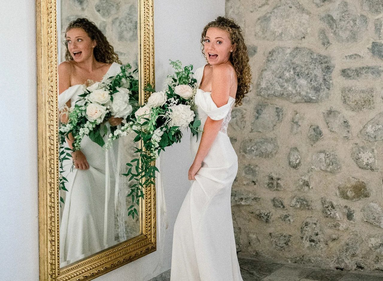 Mariée riant devant un miroir doré au Mas des 5 Fontaines, robe épaules dénudées