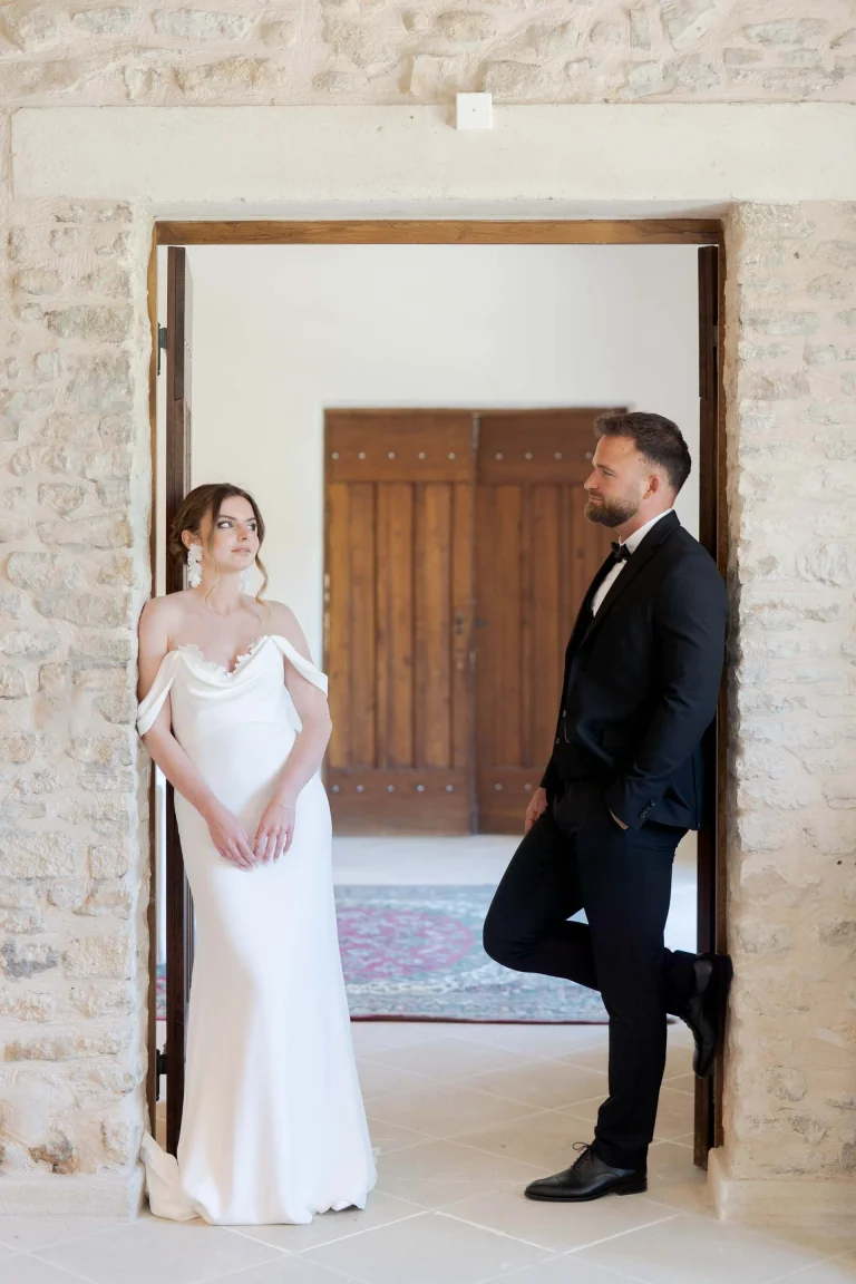 Mariée en robe Lolette épaules dénudées et marié sous une porte en pierre