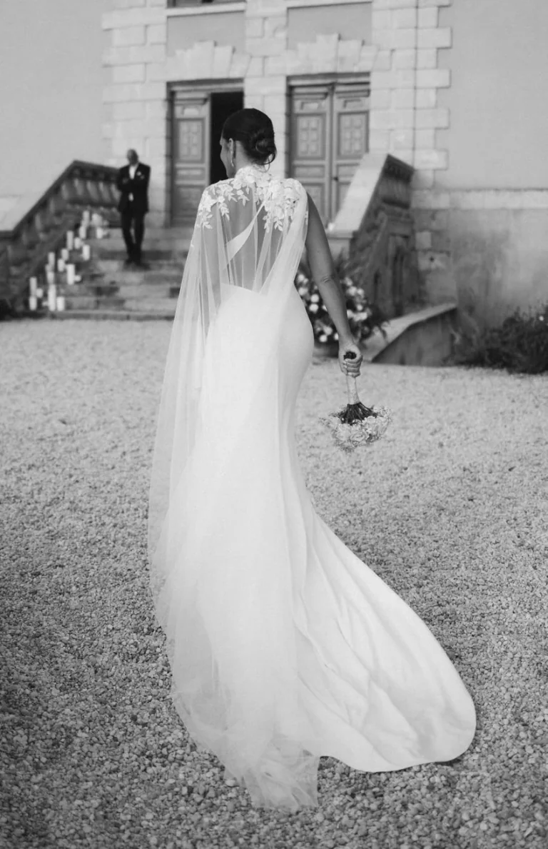 Mariée de dos avec un long voile, devant un château, en noir et blanc