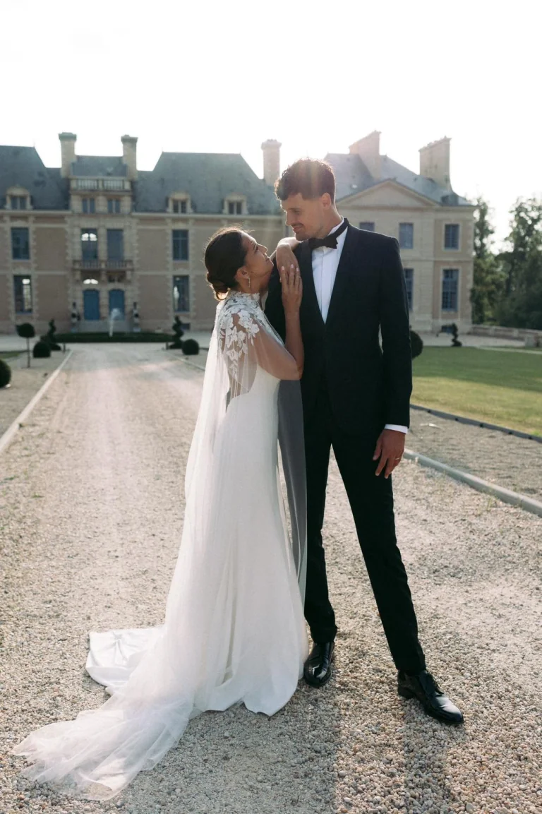 Mariée en cape de dentelle et marié devant un château