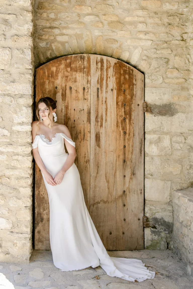 Mariée en robe Lolette épaules dénudées devant une porte en bois ancienne