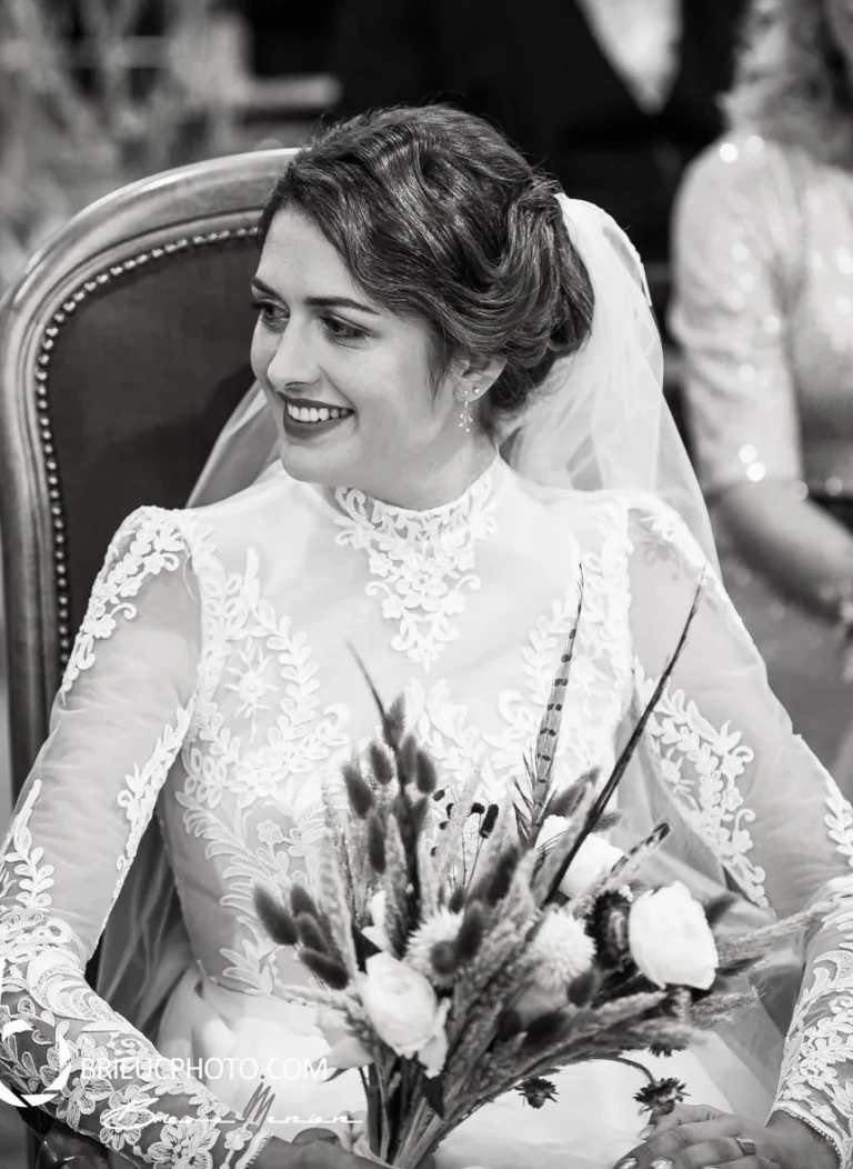 Mariée souriante en robe à col montant et manches en dentelle, en noir et blanc