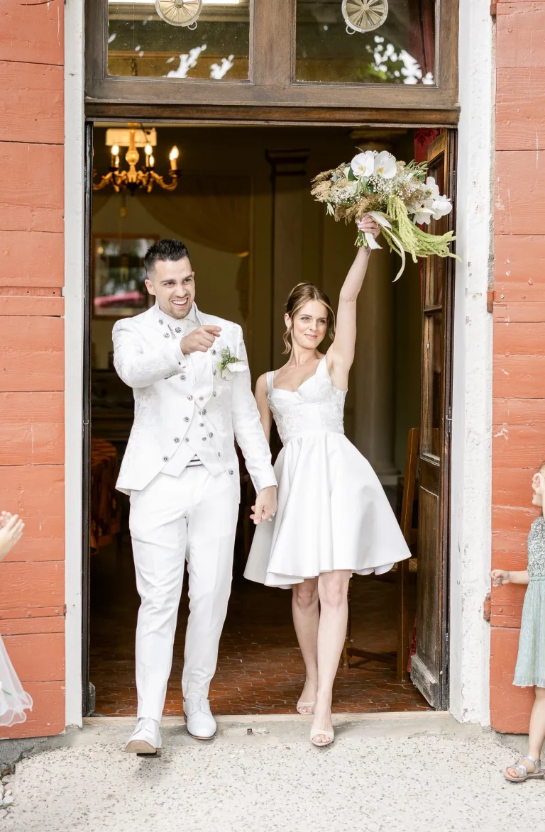 Sortie de mairie joyeuse, mariée en robe courte levant son bouquet