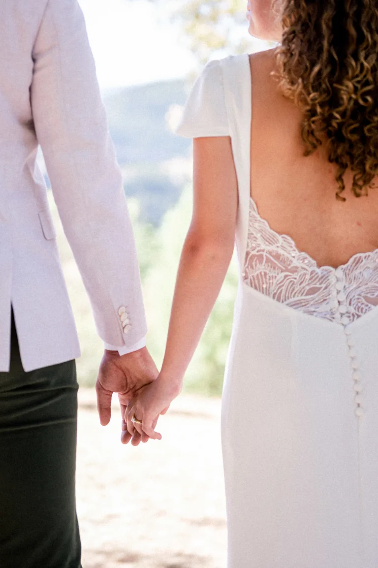 Mains des mariés jointes, dos en dentelle boutonné et manches courtes