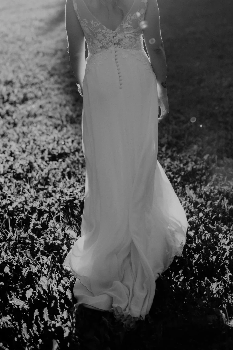 Mariée de dos dans l'herbe, robe à dos boutonné, en noir et blanc