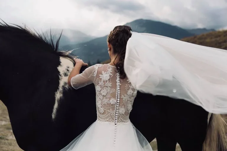 Mariée caressant un cheval noir, dos en dentelle boutonné et long voile