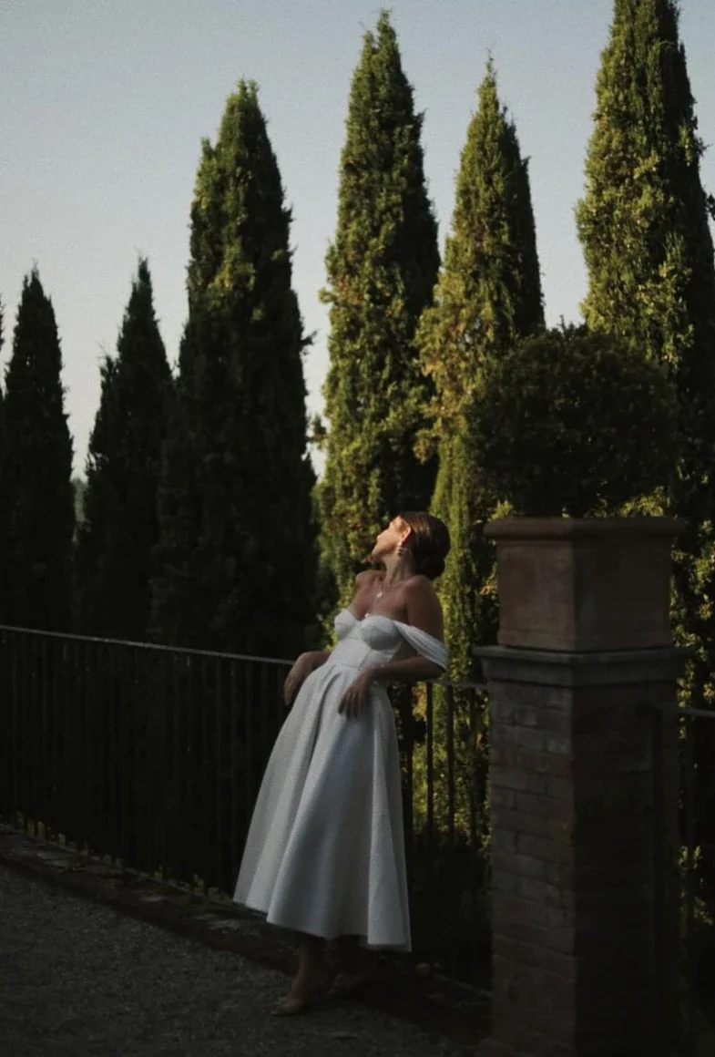 Entre les cyprès toscans Mariée accoudée à une grille entre les cyprès, robe sur mesure en satin de soie