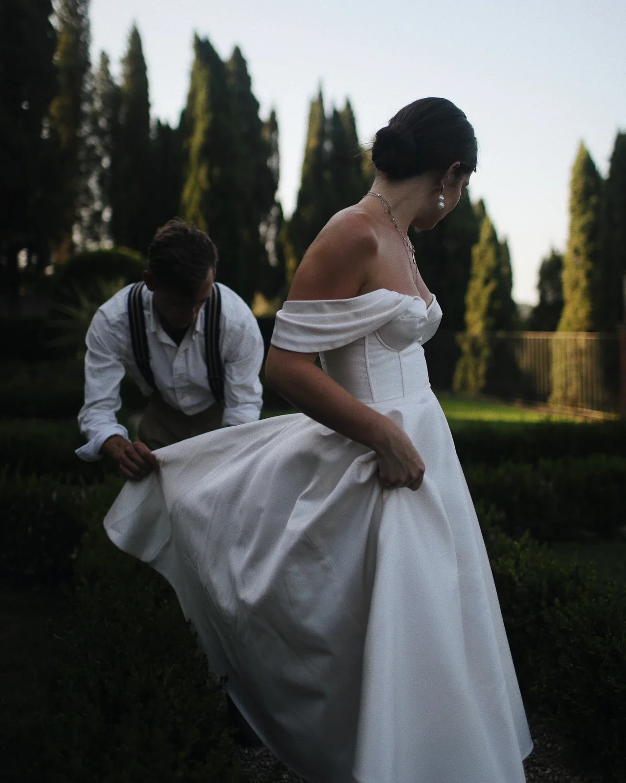 Le marié ajuste la jupe de la robe dans un jardin toscan