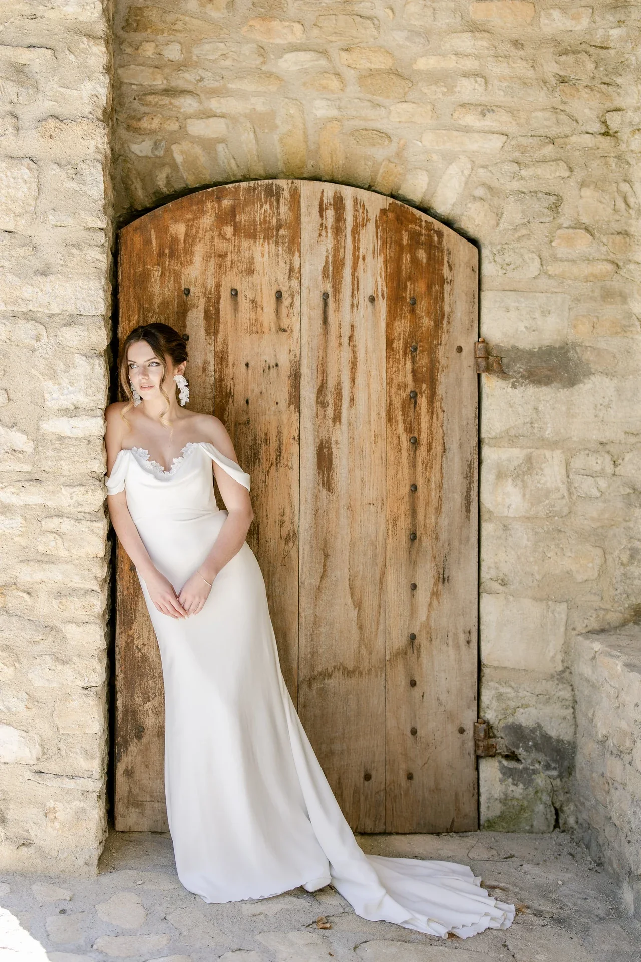 Mariée en robe épaules dénudées sous une porte en bois du Château du Griffon