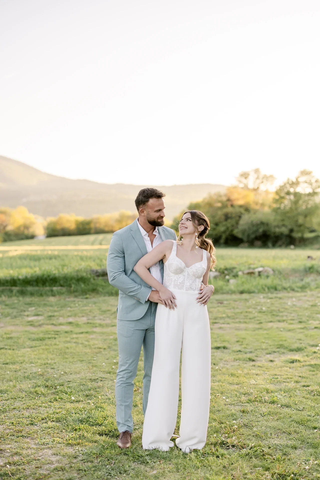 Mariée en combinaison à bustier enlacée par le marié dans un pré du Luberon